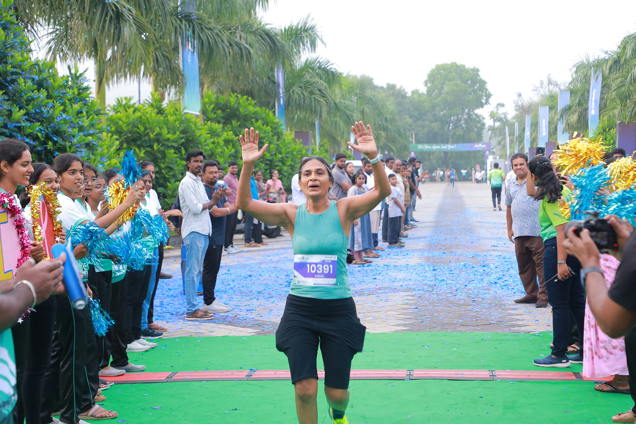 A second-edition runner reaches the finish area between cheering volunteers.