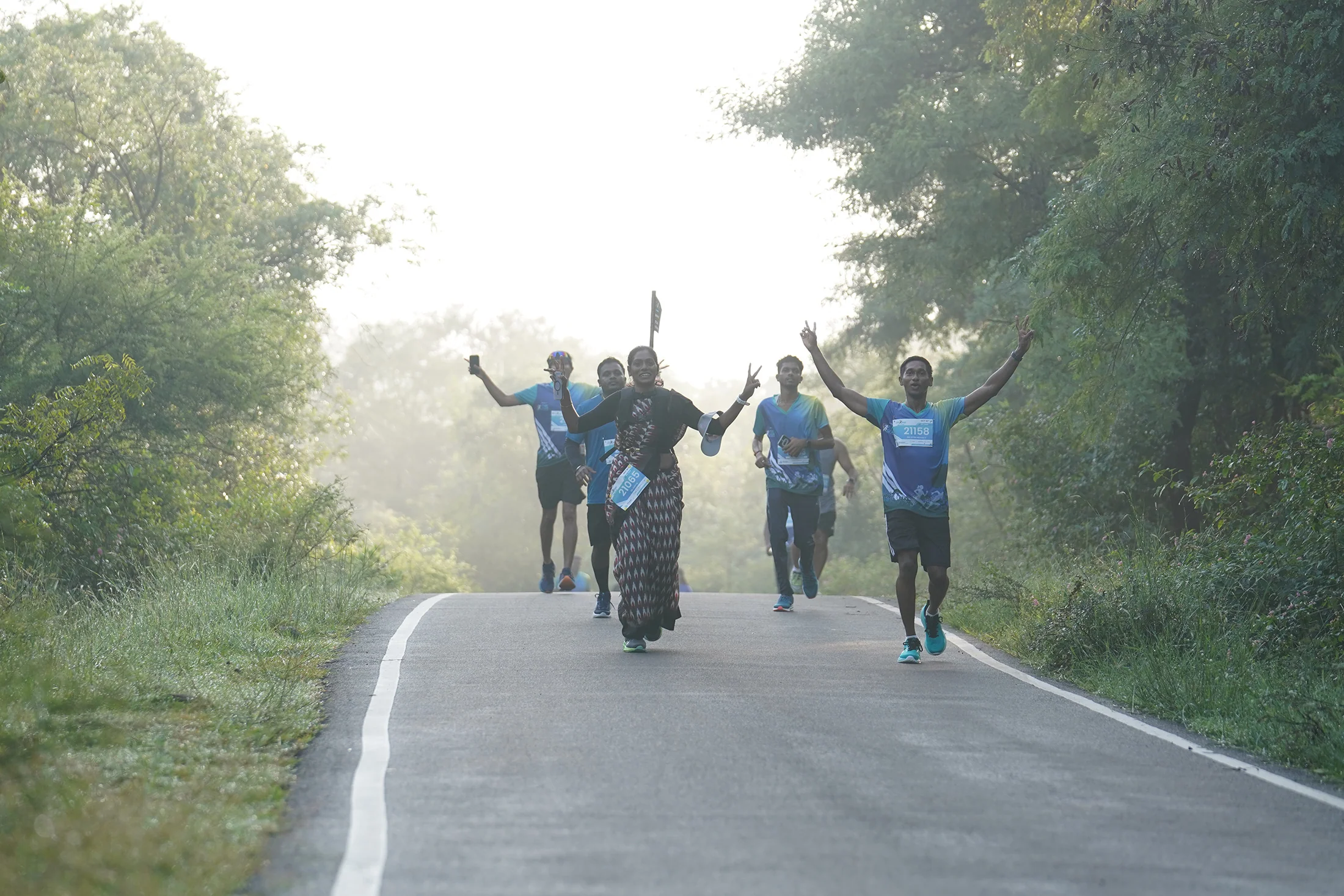 Runners raising their arms on the wooded road in 2025.