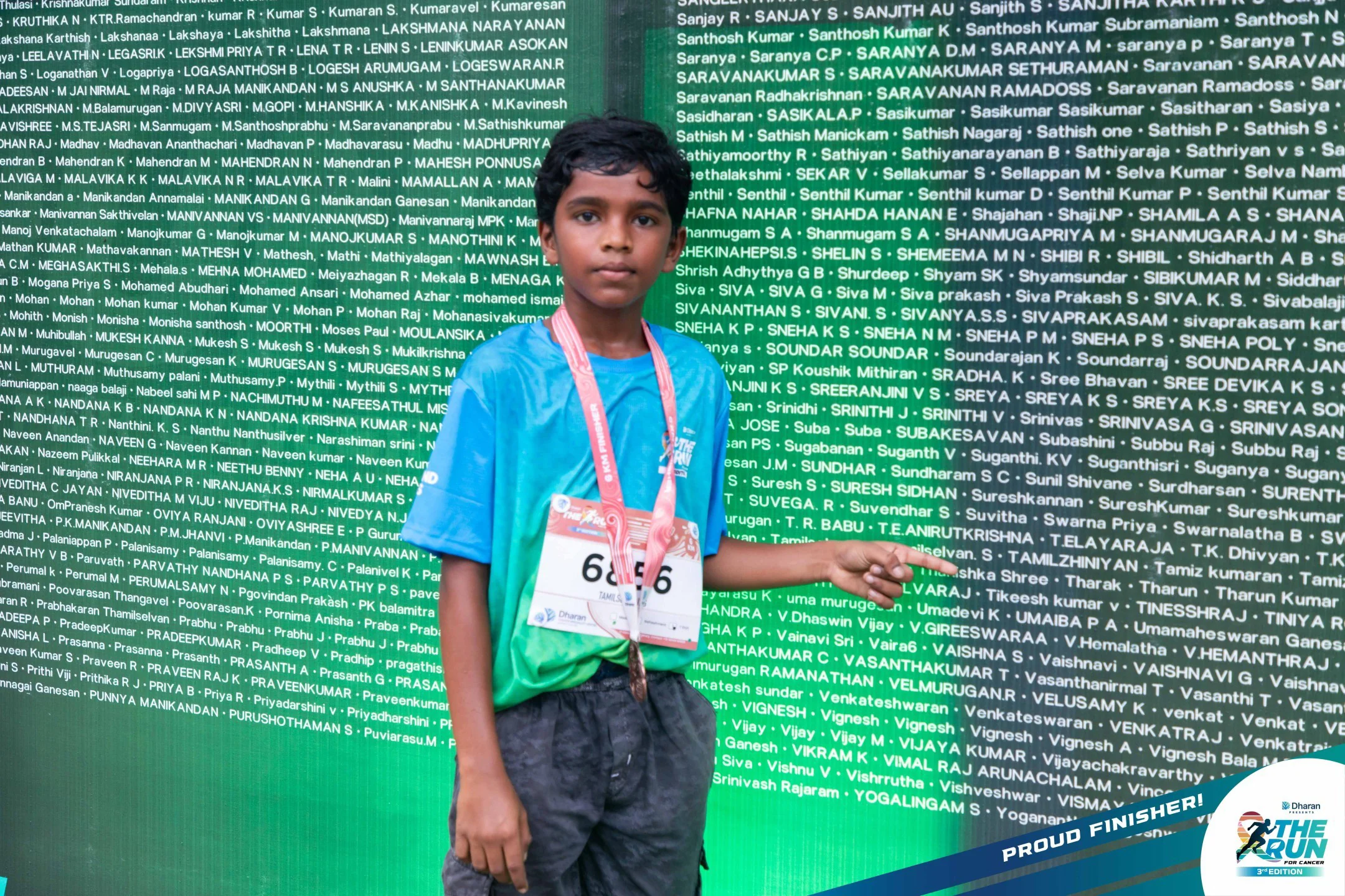A young finisher points to his name on the physical 2026 runner wall.