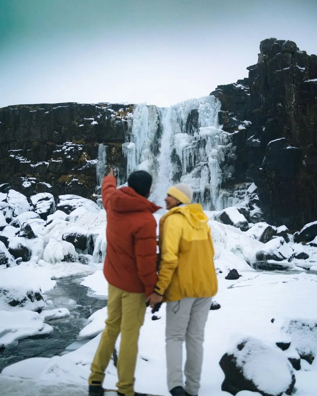 Couple in colourful jackets at a frozen waterfall